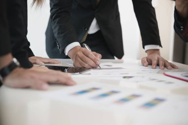 İş adamlarının eli ofis masasında iş evrakları yazıyor. Bir grup insan iş analizi yapıyor. Beyin fırtınası, takım çalışması, toplantı konsepti.