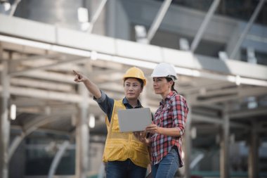 Asya mühendisler grubu dizüstü bilgisayar ve planı kağıt basılı tutarak çalışma sitesi yapı inşaat bakın. Şehir arka planda. Teknoloji, ekip çalışması kavramı
