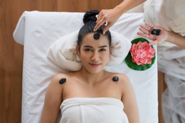 Üst Manzara. Kadın masörün eli taşı Asyalı bir kızın yüzüne yerleştirirken gülümse ve kaplıca salonunda uyu. Güzellik tedavisi ve rahatlatıcı konsept. Spa Sıcak Taşları