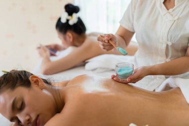 Masözün eli, tuzlu masaj yaptırırken Asyalı genç bir kadın kaplıcada dinlenirken arkaya tuz serpiyor. sağlıklı yaşam tarzı ve rahatlama kavramı