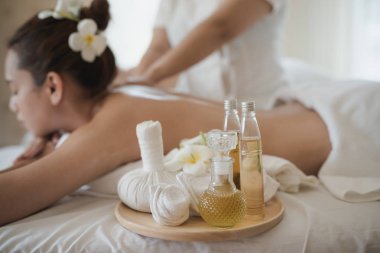 Ahşap tepside bir şişe gerekli yağ. Arka planda güzel bir Asyalı kadın masaj odasında dinleniyor.