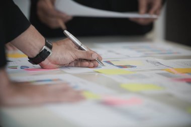 İş adamının eli Veri Tabloları 'nda kalemle yazı yazıyor. Ofis masasında belge var. Beyin fırtınası analizi, toplantı konsepti.