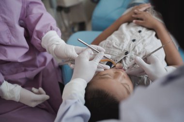Diş hekiminin elleri diş aletini tutuyor. Hastanedeki dişçi koltuğunda yatan çocuğun dişlerini kontrol ediyorum..