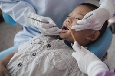 Diş hekiminin elleri diş aletini tutuyor. Hastanedeki dişçi koltuğunda yatan çocuğun dişlerini kontrol ediyorum..