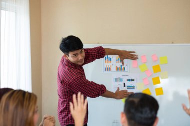 Odanın önünde dikilen sıradan ekose gömlekli genç Asyalı erkekler, konferansta başarılı bir iş yürütme konusunda meslektaşlarından geri bildirim istiyor. Takım çalışması iş toplantısı