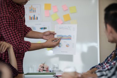 Odanın önünde dikilen sıradan ekose gömlekli genç Asyalı erkekler, konferansta başarılı bir iş yürütme konusunda meslektaşlarından geri bildirim istiyor. Takım çalışması iş toplantısı