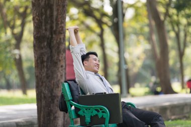 Asyalı iş adamı işten sonra parkta dinleniyor. Güneşli bir günde ağacın gölgesinin tadını çıkarıyorum. İş adamı rahatlatma, dinlenme zamanı kavramı