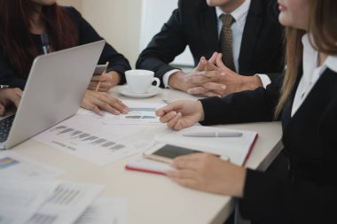Asyalı genç iş adamları ve kadın grupları ofis masasında borsa çizelgeleri üzerinde tartışıyorlar. İş analizi yapıyorlar. İşyerinde kullanılmış bir laptop. Beyin fırtınası, takım çalışması, toplantı konsepti.