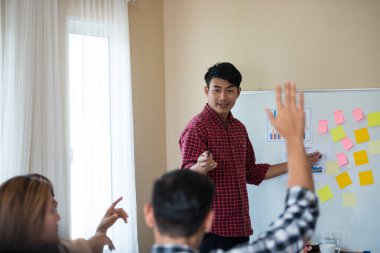 Odanın önünde dikilen sıradan ekose gömlekli genç Asyalı erkekler, konferansta başarılı bir iş yürütme konusunda meslektaşlarından geri bildirim istiyor. Takım çalışması iş toplantısı