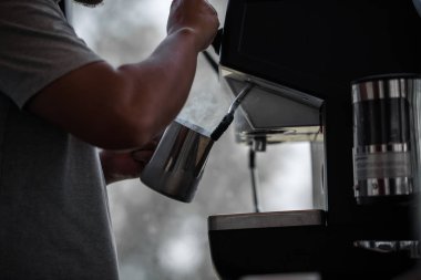 Adam kahve makinesiyle kahve yapıyor. Kafede sıcak buhar kullanıyor.