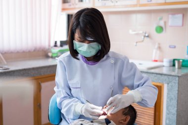 Diş hekimi diş aletini tutuyor. Hastanedeki dişçi koltuğunda yatan çocuğun dişlerini kontrol ediyorum..