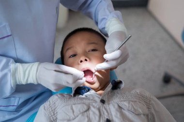 Diş hekiminin elleri diş aletini tutuyor. Hastanedeki dişçi koltuğunda yatan çocuğun dişlerini kontrol ediyorum..