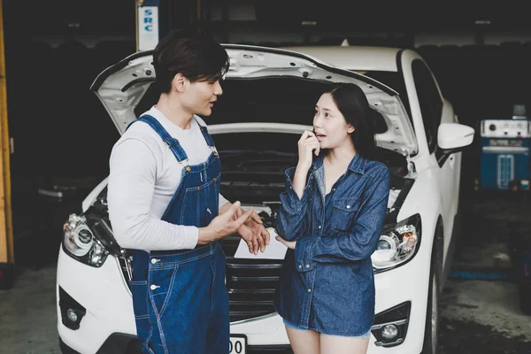 Young mechanic talk about repair car to woman or owner at car shop. agreement in repair service check the car.