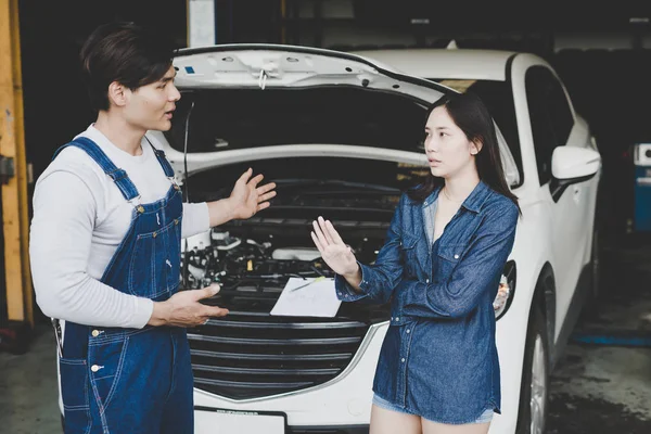 Young mechanic talk about repair car to woman or owner at car raise the hands rejecting disagree. agreement in repair service check the car.