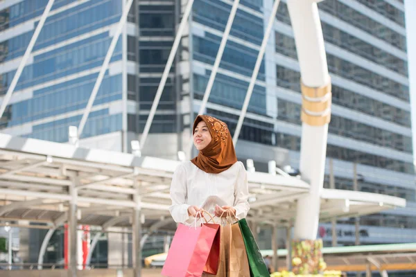 Beautiful malaysia young woman a smiling and happy with shopping bags,  lifestyle concept in the big city, the business district with skyscrapers in the Background
