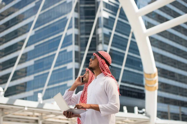 两名阿拉伯商人使用笔记本电脑和手机在大城市 商业区与摩天大楼的背景 用于添加文本消息的图片 设计艺术作品背景 — 图库照片