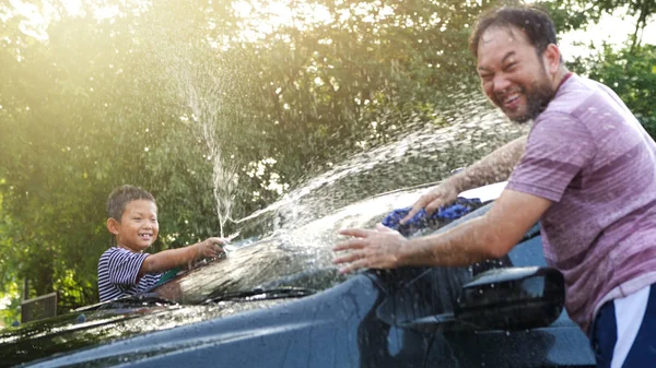 Happy Asian boy help parent washing car on water splashing with sunlight at home, Slow Motion. Activity holidays in family.