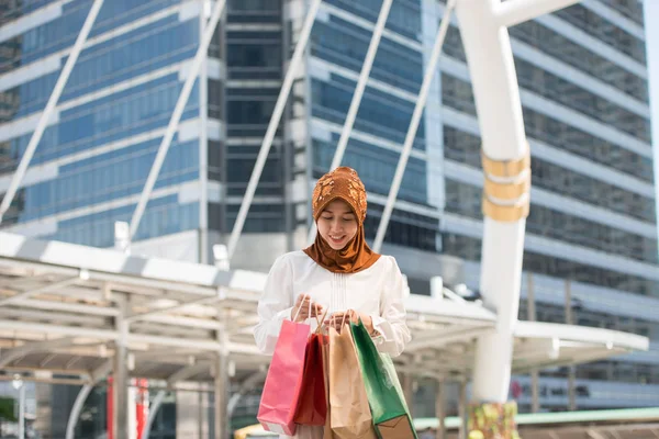 Bir gülümseyen güzel Malezya genç kadın ve mutlu alışveriş torbaları, büyük şehirde yaşam tarzı kavramı, gökdelenler içinde belgili tanımlık geçmiş ile iş merkezleri ile
