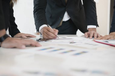 İş adamlarının eli ofis masasında iş evrakları yazıyor. Bir grup insan iş analizi yapıyor. Beyin fırtınası, takım çalışması, toplantı konsepti.