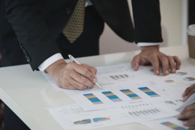 İş adamının eli Veri Tabloları 'nda kalemle yazı yazıyor. Ofis masasında belge var. Beyin fırtınası analizi, toplantı konsepti.