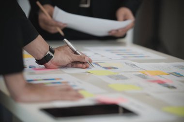 İş adamının eli Veri Tabloları 'nda kalemle yazı yazıyor. Ofis masasında belge var. Beyin fırtınası analizi, toplantı konsepti.
