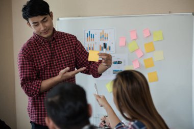 Odanın önünde dikilen sıradan ekose gömlekli genç Asyalı erkekler, konferansta başarılı bir iş yürütme konusunda meslektaşlarından geri bildirim istiyor. Takım çalışması iş toplantısı