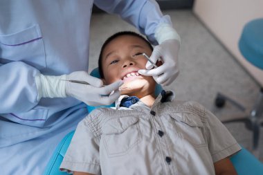 Diş hekiminin elleri diş aletini tutuyor. Hastanedeki dişçi koltuğunda yatan çocuğun dişlerini kontrol ediyorum..