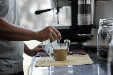 Elinde kaşık kullanarak sıcak su ve kahveyle karıştıran bir erkek barista.