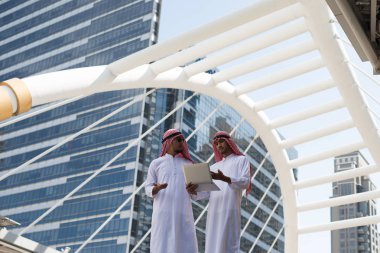 İki genç Arap işadamı, Bangkok şehrinin arka planında dizüstü bilgisayarla çalışırken konuşuyorlardı.