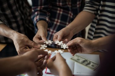 Yapboz beyazını birleştiren bir grup iş adamı. Aşağıda toplantı odasındaki ahşap masaya yerleştirilmiş grafik kağıtları var..