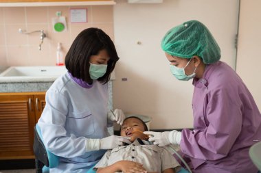 Diş hekimi diş aletini tutuyor. Hastanedeki dişçi koltuğunda yatan çocuğun dişlerini kontrol ediyorum..