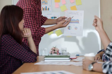 Odanın önünde dikilen sıradan ekose gömlekli genç Asyalı erkekler, konferansta başarılı bir iş yürütme konusunda meslektaşlarından geri bildirim istiyor. Takım çalışması iş toplantısı