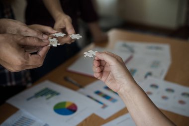 Yapboz beyazını birleştiren bir grup iş adamı. Aşağıda toplantı odasındaki ahşap masaya yerleştirilmiş grafik kağıtları var..