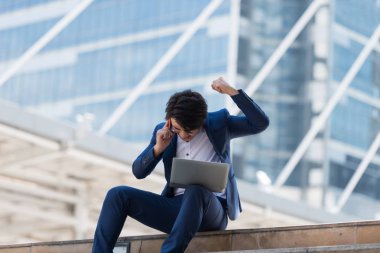 Genç Asyalı iş adamı ciddi bir yüzle cep telefonuyla konuşuyor ve Bangkok Tayland 'da dizüstü bilgisayarında çalışıyor. İletişim kavramı