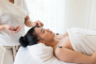 Genç ve güzel Asyalı kadın spa 'da mineral taşıyla yüz masajı yaptırıyor.