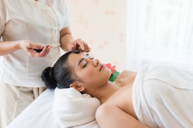 Genç ve güzel Asyalı kadın spa 'da mineral taşıyla yüz masajı yaptırıyor.