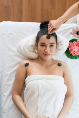 Genç ve güzel Asyalı kadın spa 'da mineral taşıyla yüz masajı yaptırıyor.