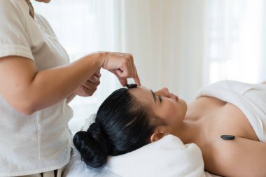 Genç ve güzel Asyalı kadın spa 'da mineral taşıyla yüz masajı yaptırıyor.