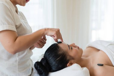 Kadın masör, taşı kaplıca salonundaki Asyalı bir kızın yüzüne yerleştirdi. Güzellik tedavisi ve rahatlatıcı konsept. Spa Sıcak Taşları