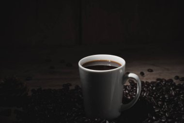 Beyaz bardakta sıcak kahve ve sehpanın üzerinde kahve çekirdekleri.