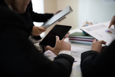 Toplantıda yapılan görüşmelerde dijital tablet, grafikler ve iş belgelerine işaret eden işadamı eli.