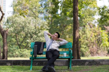 Asyalı iş adamı işten sonra parkta dinleniyor. Güneşli bir günde ağacın gölgesinin tadını çıkarıyorum. İş adamı rahatlatma, dinlenme zamanı kavramı