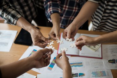 Yapboz beyazını birleştiren bir grup iş adamı. Aşağıda toplantı odasındaki ahşap masaya yerleştirilmiş grafik kağıtları var..