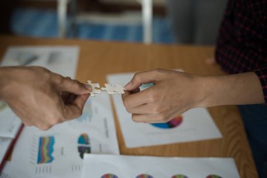 İş adamlarının yapboz yapbozunu beyaza çevirmesi. Aşağıda toplantı odasındaki ahşap masaya yerleştirilmiş grafik kağıtları var..