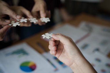 Yapboz beyazını birleştiren bir grup iş adamı. Aşağıda toplantı odasındaki ahşap masaya yerleştirilmiş grafik kağıtları var..