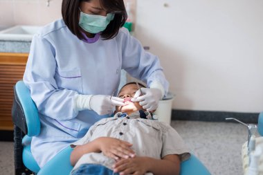 Diş hekimi diş aletini tutuyor. Hastanedeki dişçi koltuğunda yatan çocuğun dişlerini kontrol ediyorum..