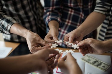 Yapboz beyazını birleştiren bir grup iş adamı. Aşağıda toplantı odasındaki ahşap masaya yerleştirilmiş grafik kağıtları var..