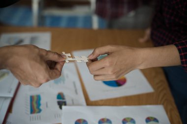 İş adamlarının yapboz yapbozunu beyaza çevirmesi. Aşağıda toplantı odasındaki ahşap masaya yerleştirilmiş grafik kağıtları var..