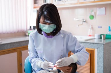 Diş hekimi diş aletini tutuyor. Hastanedeki dişçi koltuğunda yatan çocuğun dişlerini kontrol ediyorum..