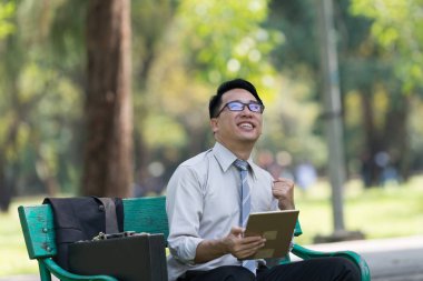 Genç işadamı parkta dijital tablet bakarak. Onların başarısı sevinç belirtileri gösteriyor. Başarılı işadamı kavramı